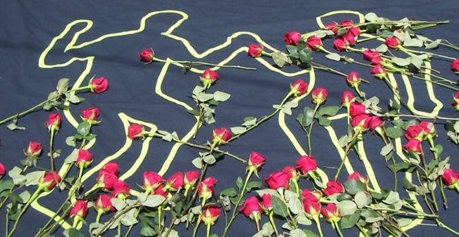 A white outline of two people on black cloth is covered in several red roses