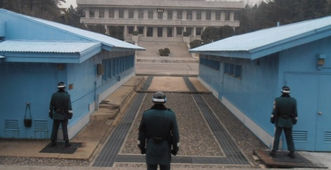 Three uniformed guards stand at their posts, facing two blue buildings