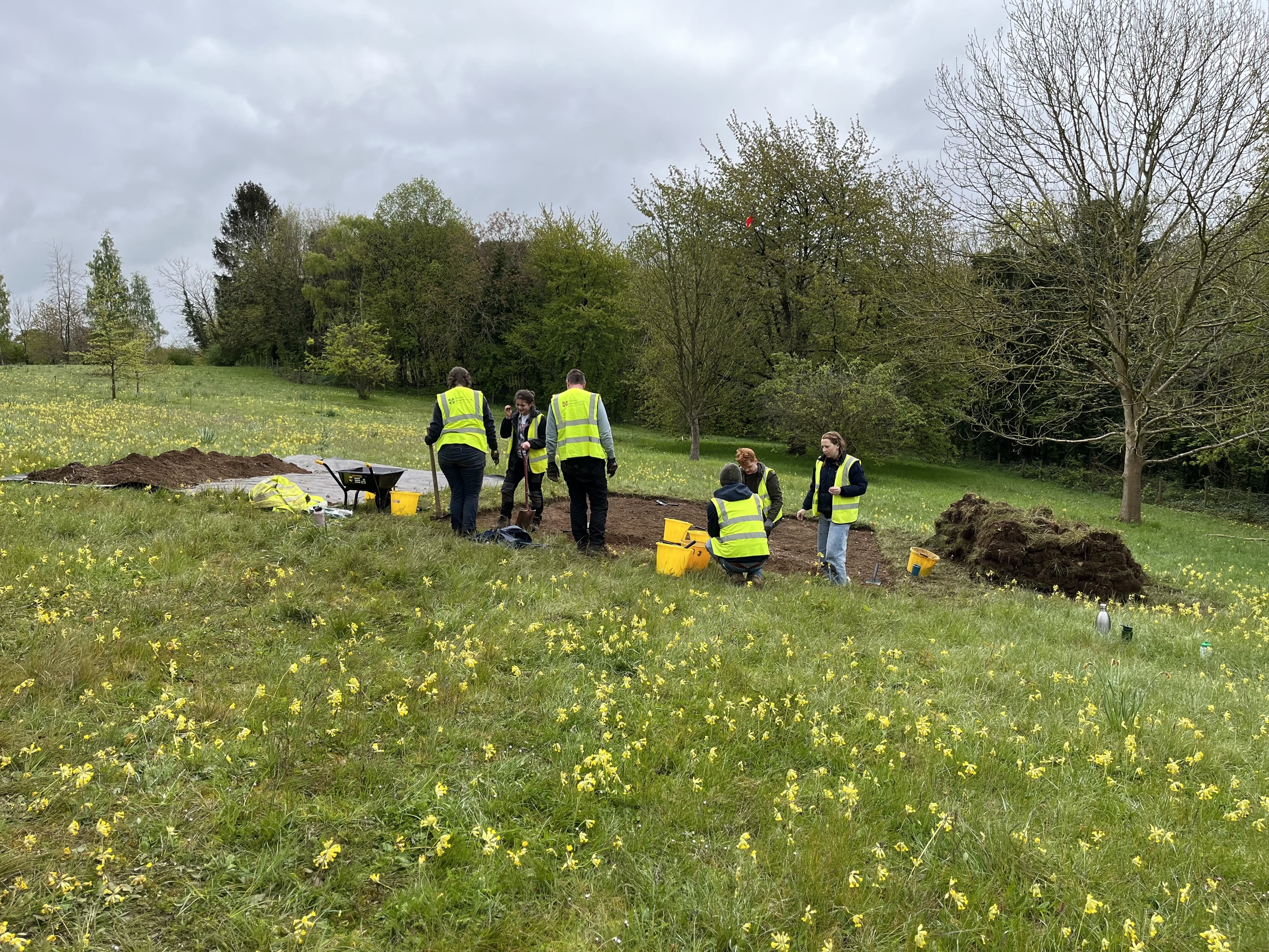 Students and staff wearing hi-vis with buckets and trowels in the pit